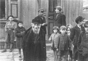 An elderly Jewish man stands among a group of children in a ghetto